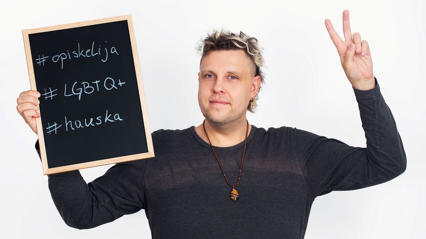 Henkilö katsoo kameraa kädet ylhäällä, toisessa kä