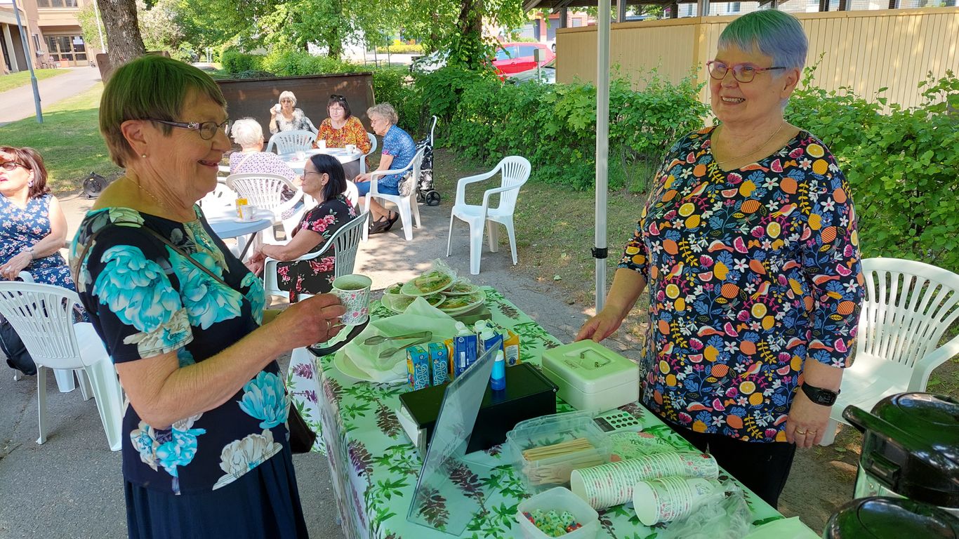 Asiakas kahvikuppi kädessä hymyilee kauppiaalle ti